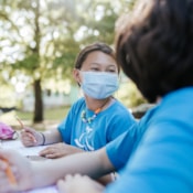 Girls on the Run participant smiles outside while wearing mask and working in her journal
